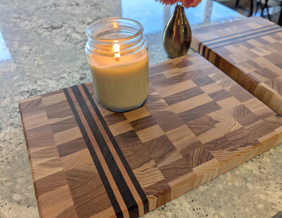End-grain cutting board with dark inlay stripes and a candle